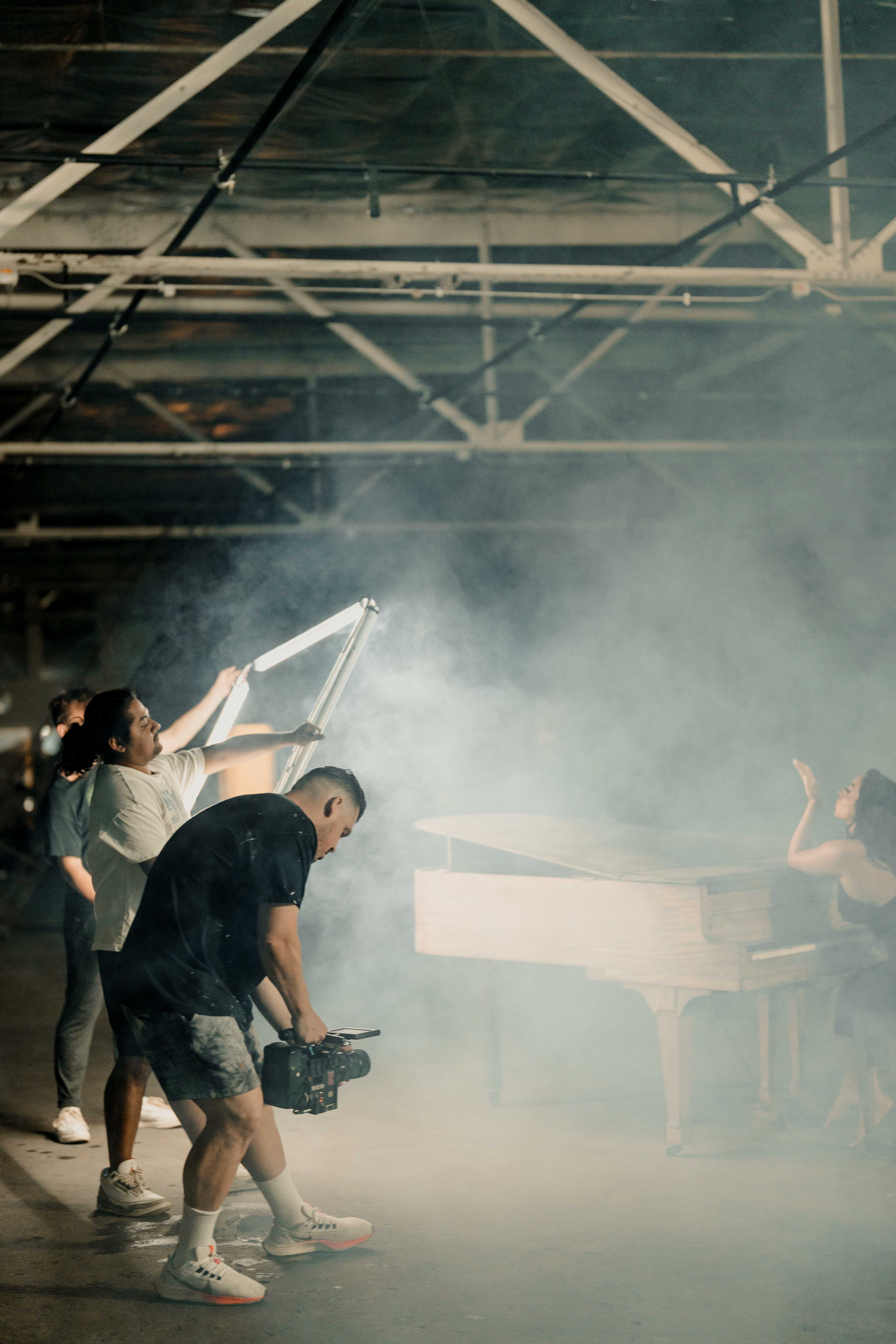 Production crew filming Bianca at the piano on a hazy warehouse set.