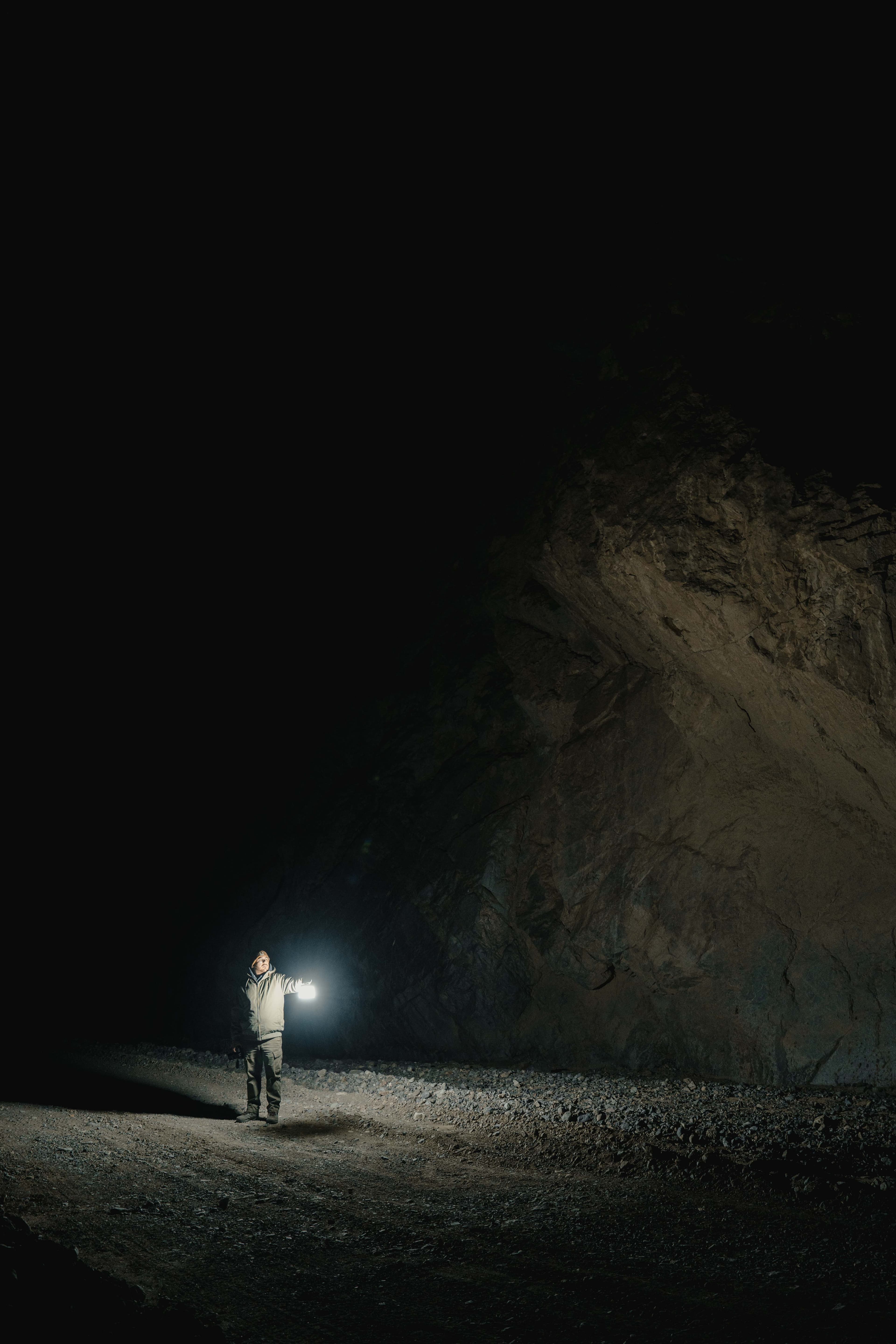 A person holding a light beneath a towering rock face at night.