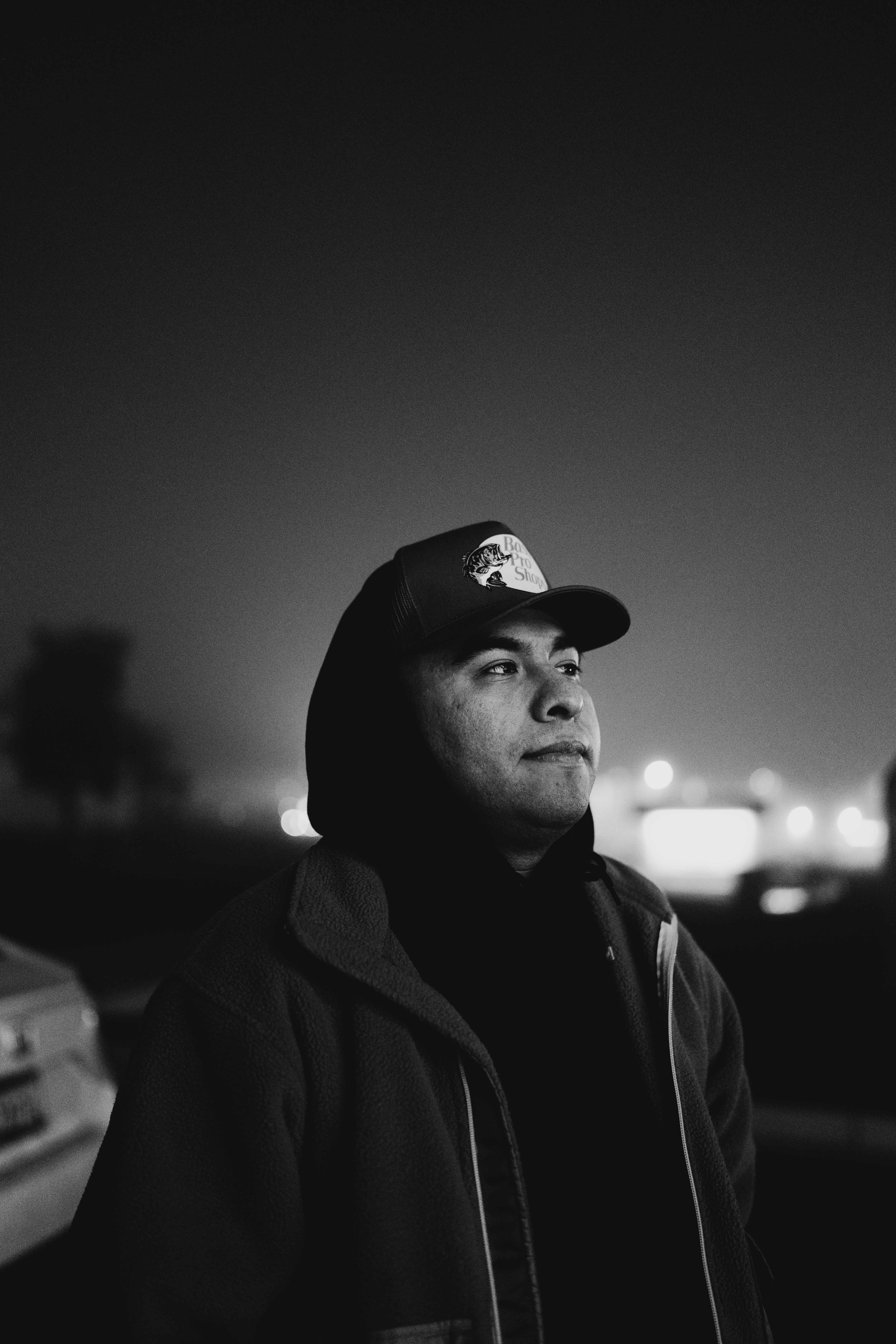 Black-and-white nighttime portrait of a man in a cap and layered jacket.