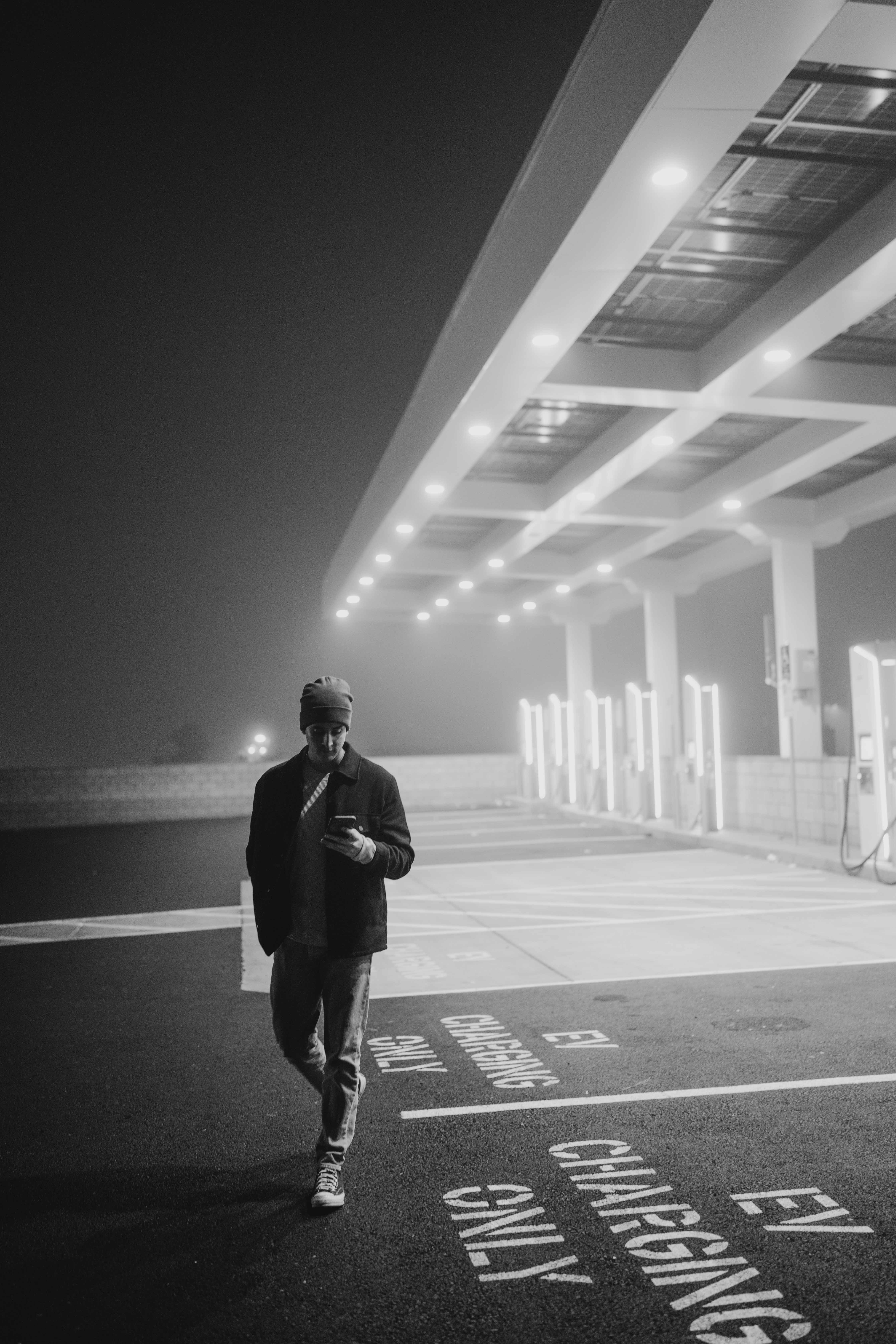 Black-and-white nighttime portrait beneath illuminated charging bays.