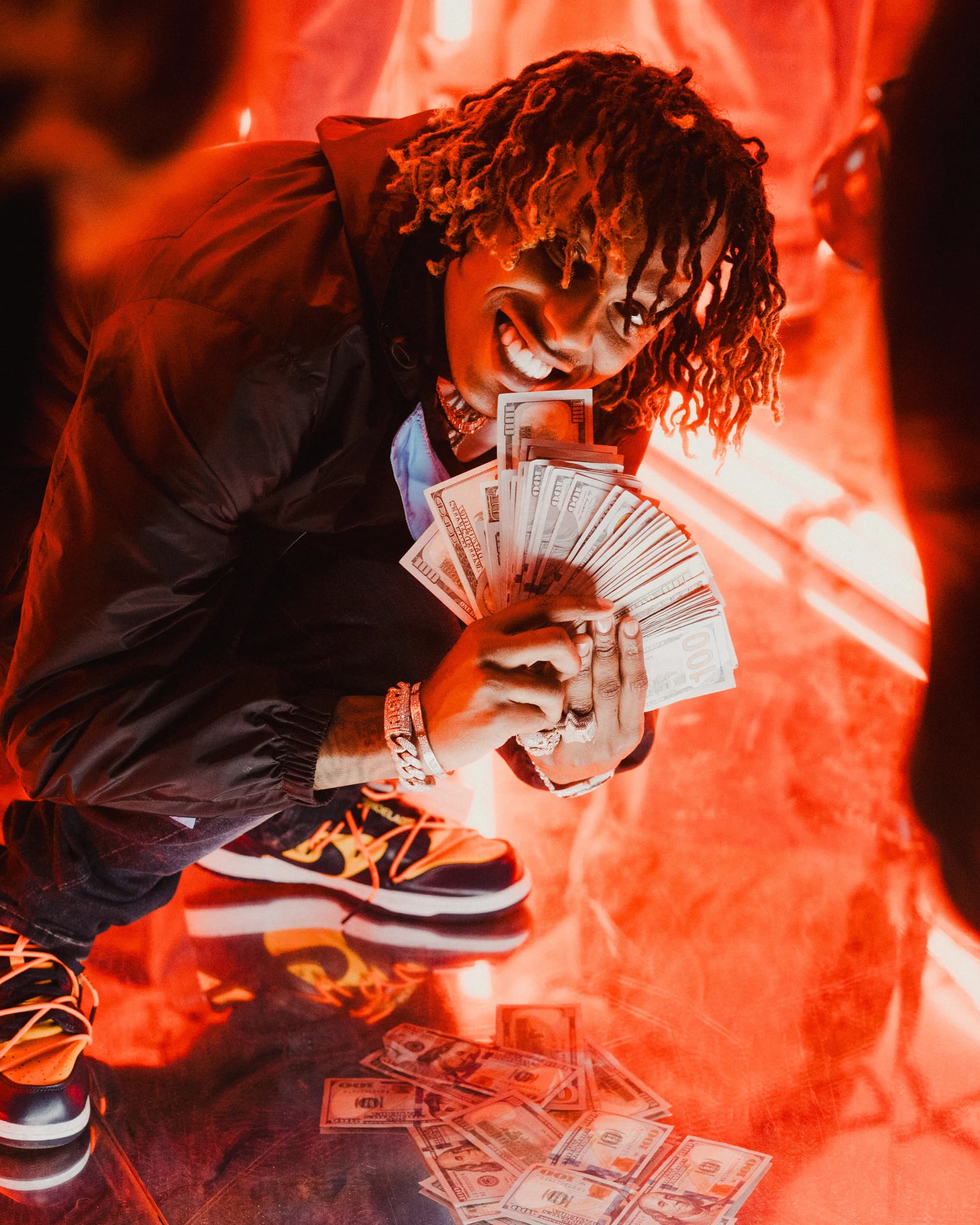 A performer crouching with a fan of banknotes in a red-lit room.