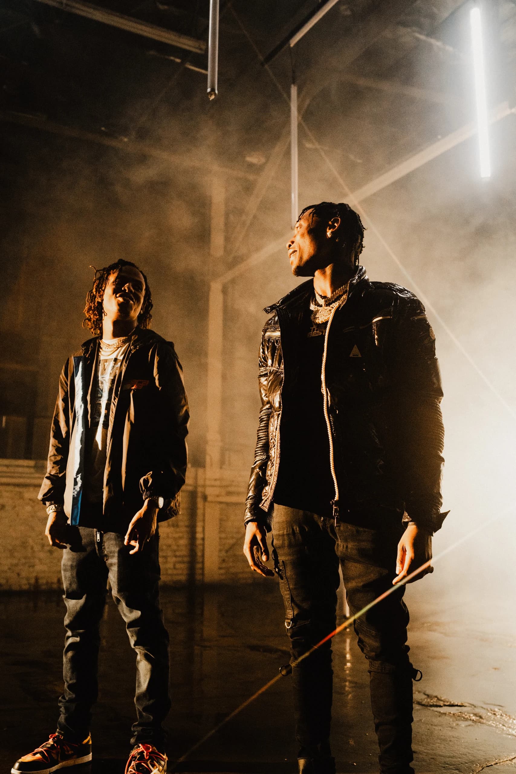 Two performers between takes in amber light and haze.