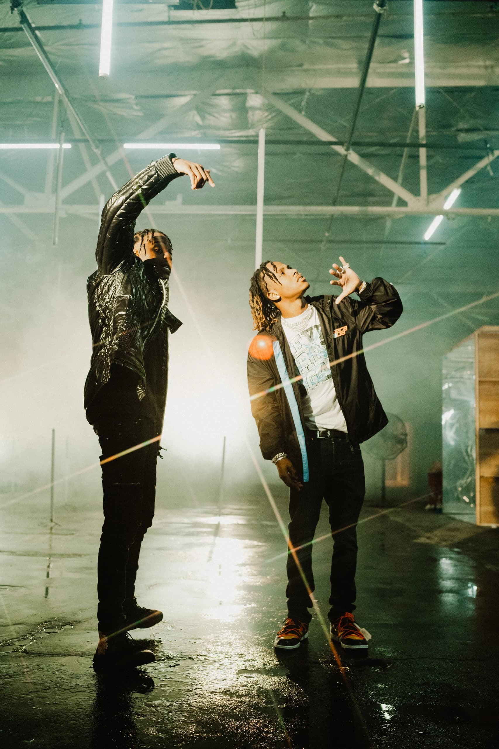 Two performers gesturing on a green-lit warehouse set.
