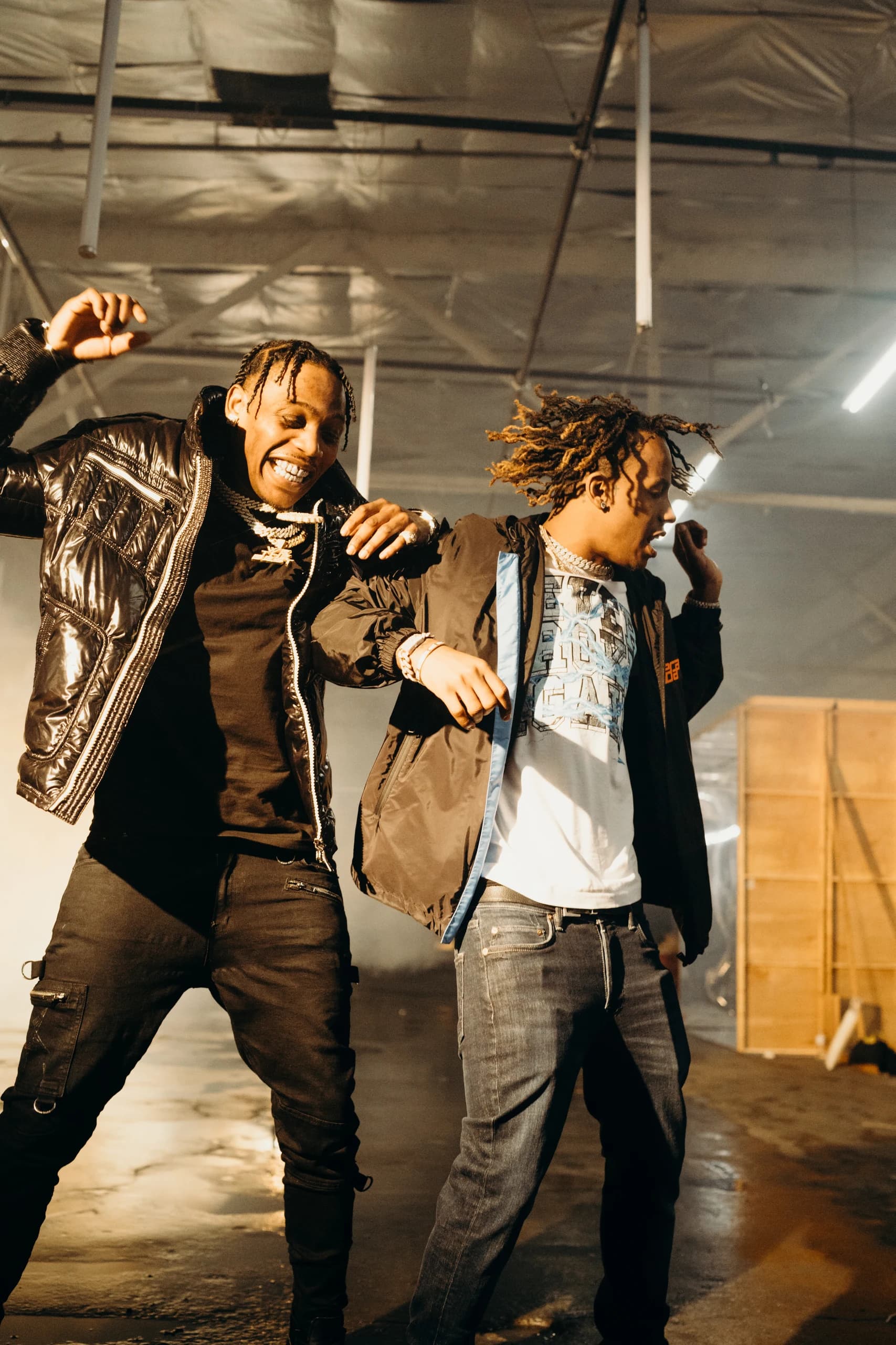 Two performers moving together under warm light on the warehouse set.