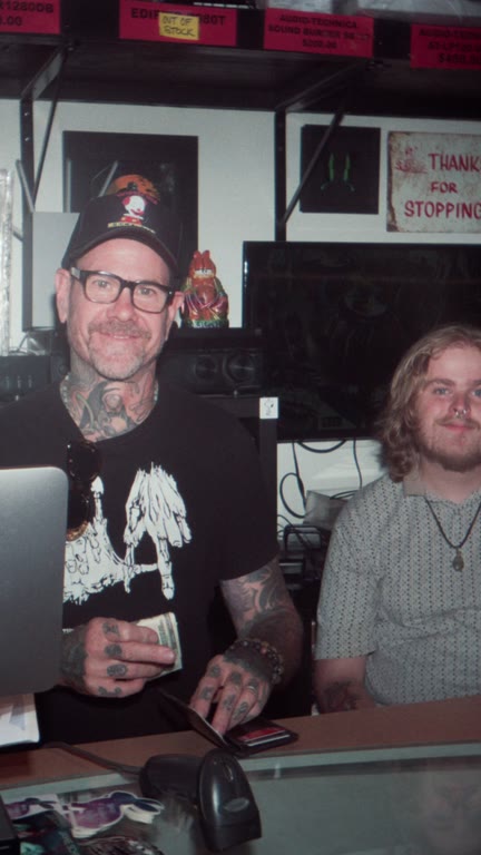 Two people behind the counter of a record shop.