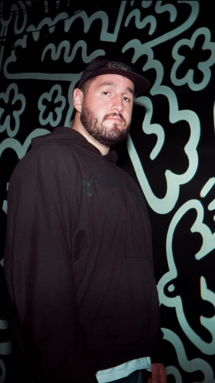 A man in a black cap standing in front of a turquoise mural.